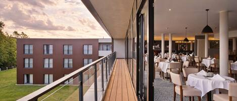 A modern outdoor dining area with a wooden deck, glass railings, and tables set for dining.