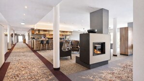 A modern hotel lobby with a central fireplace, a bar area, and a seating area with a patterned carpet. - Santé Royale Hotel & Gesundheitsresort Bad Langensalza (Bad Langensalza)