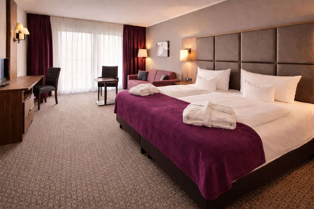 A hotel room with two beds, a desk, a chair, and a TV.