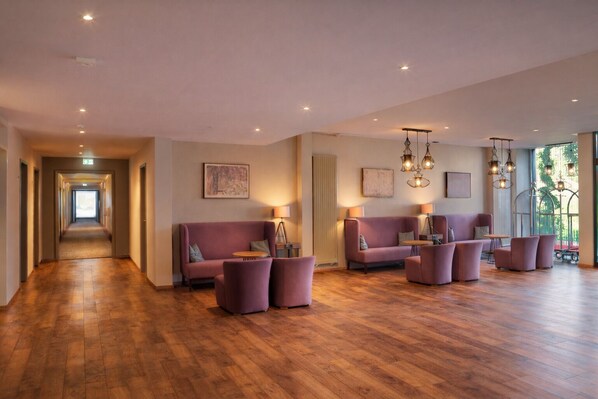 A spacious lobby with a wooden floor, a central seating area with sofas and armchairs, and pendant lighting.