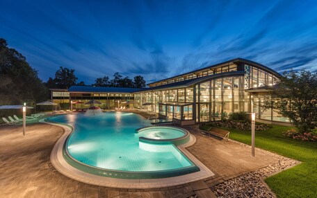 A modern pool area with a curved design, surrounded by a glass building and a well-maintained lawn.