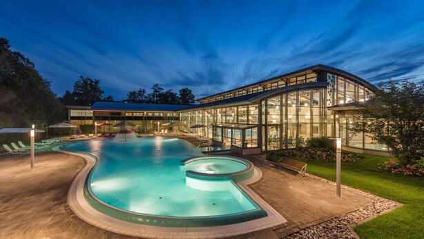 A modern pool area with a curved design, surrounded by a glass building and a well-maintained lawn. - Santé Royale Hotel & Gesundheitsresort Bad Langensalza (Bad Langensalza)