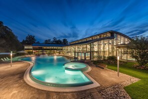 A modern pool area with a curved design, surrounded by a glass building and a well-maintained lawn.