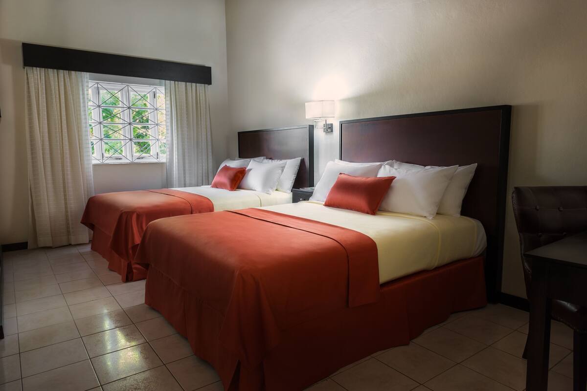 Una habitación de hotel con dos camas, una ventana con cortinas, una mesita de noche y una silla.