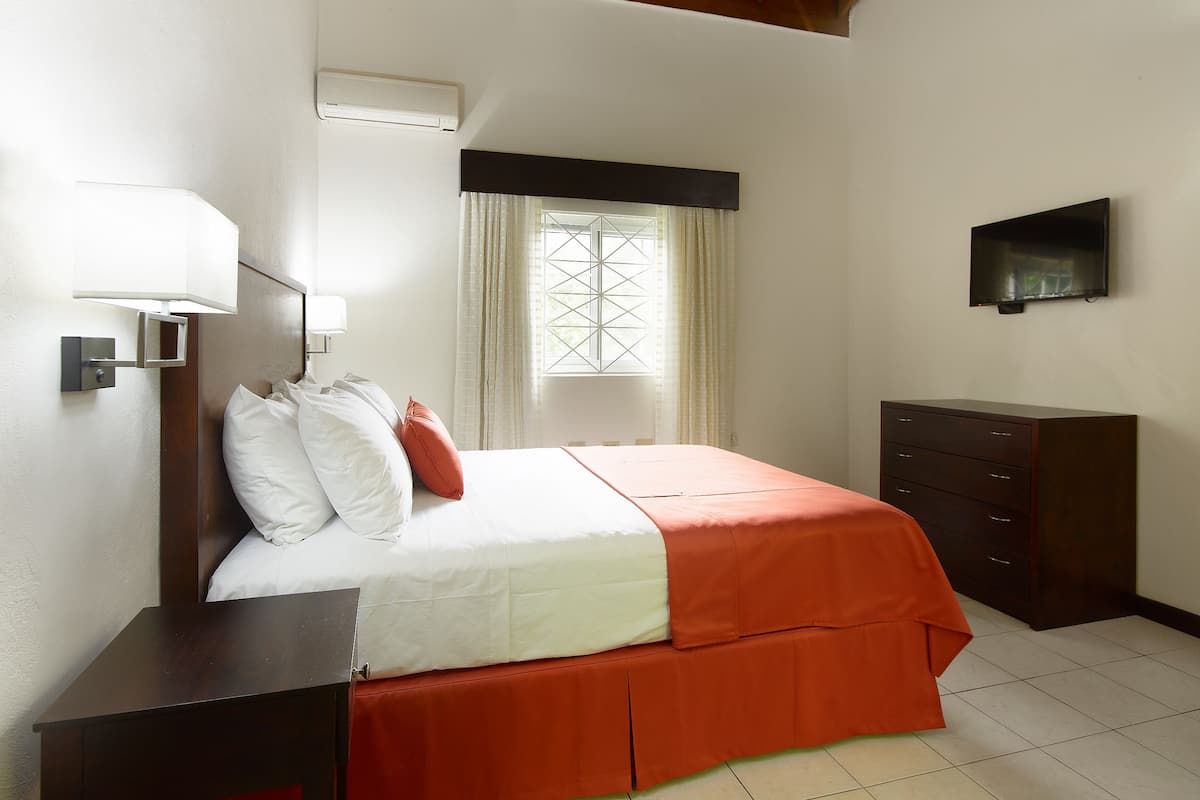 Una habitación de hotel con cama, cómoda, televisor y ventana con cortinas.