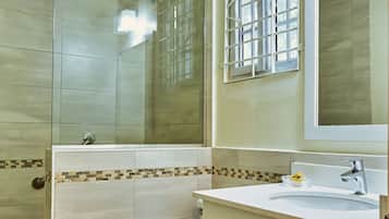 Une salle de bain avec une douche à parois de verre, des toilettes, un lavabo avec un miroir et une fenêtre à motifs géométriques.