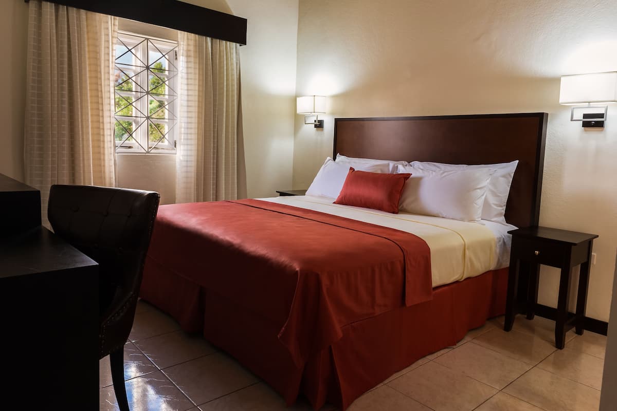 Una habitación de hotel con cama, escritorio, silla y ventana con cortinas.