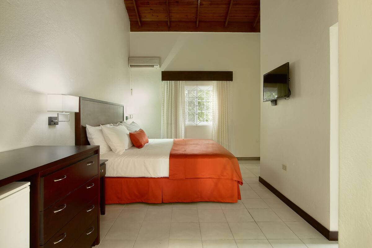 Una habitación de hotel con cama, cómoda, televisor y ventana con cortinas.