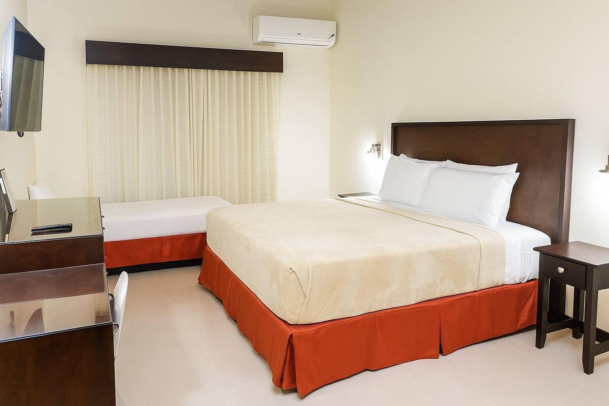 Habitación de hotel con una cama grande, una mesita de noche, un escritorio con silla y una ventana con cortinas.