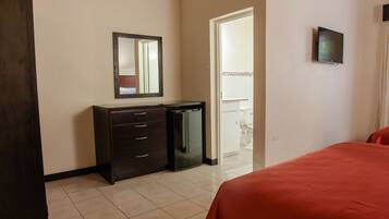 Una habitación de hotel con una cama, un tocador, un espejo, un televisor y una puerta que da a un baño.