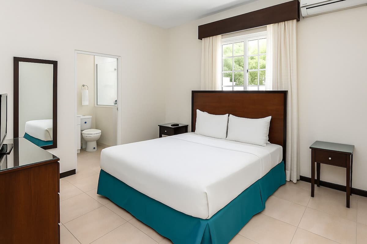 Habitación de hotel con una cama grande, una mesita de noche, un espejo, un televisor, una ventana con cortinas y un inodoro.