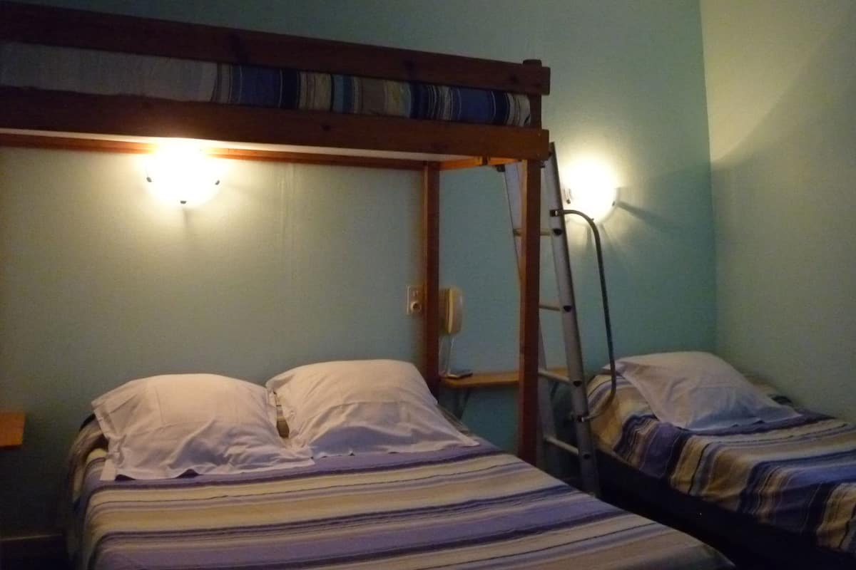 A bunk bed room with a ladder, a wall-mounted light, and a plain wall.