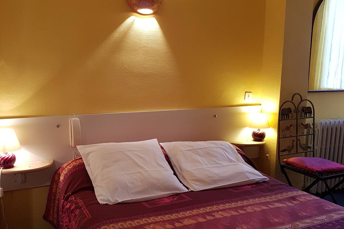A bed with white pillows and a red patterned bedspread in a room with yellow walls.