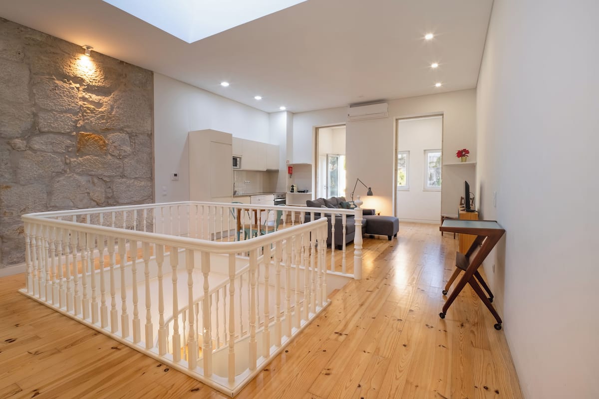 A spacious living area with a high ceiling, a staircase, and a kitchen in the background.