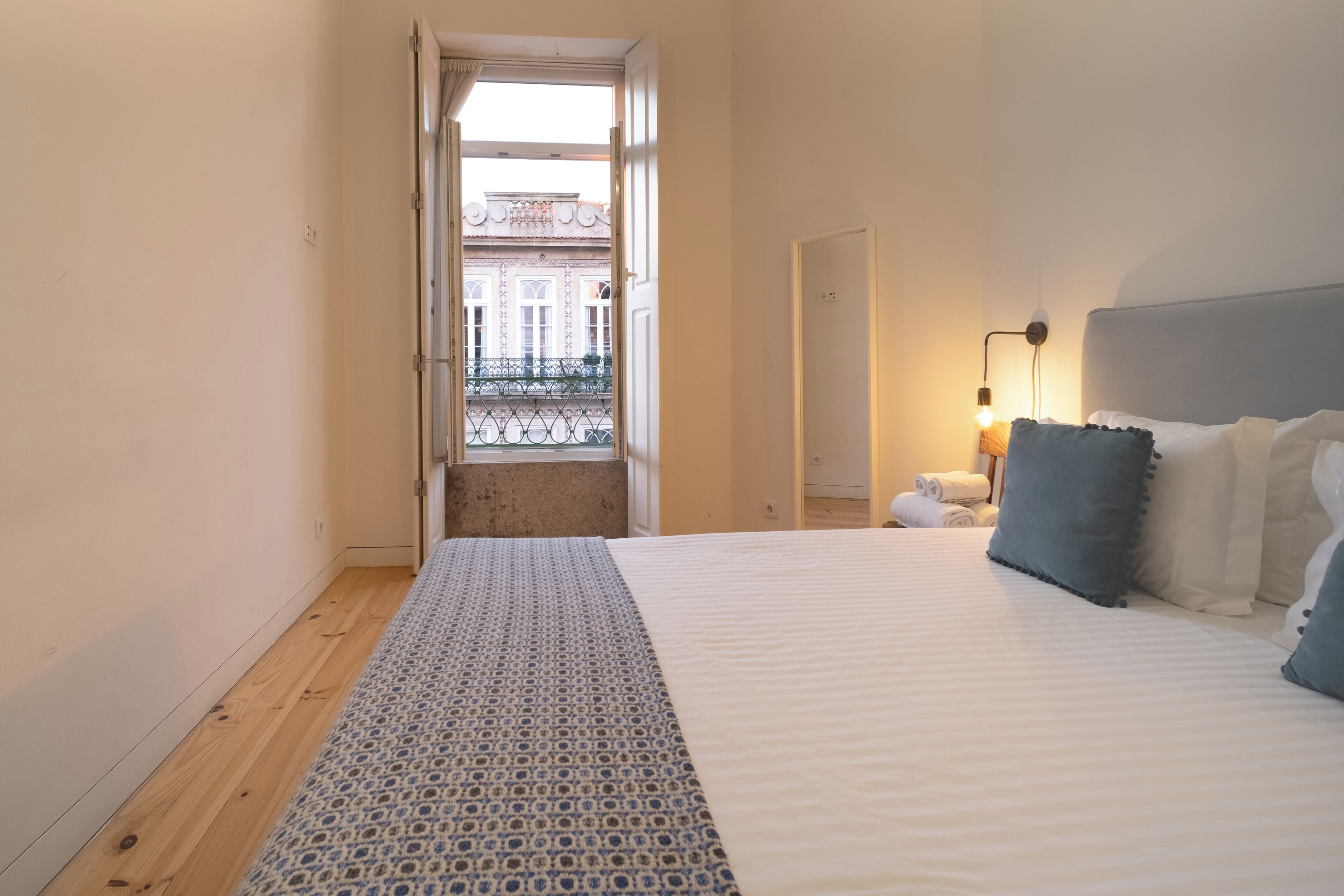 Een slaapkamer met een bed, een bedlampje en uitzicht op een balkon.