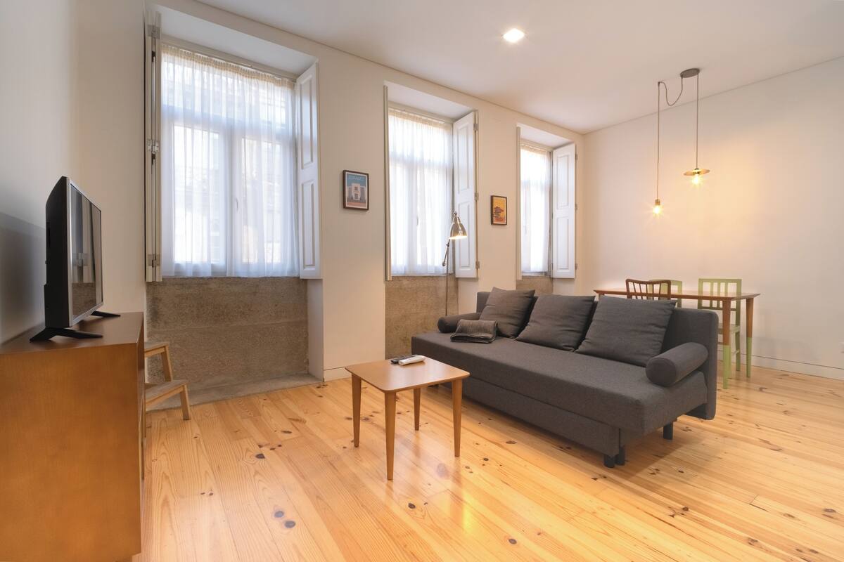 A living room with a sofa, a coffee table, a TV, and a wooden floor.