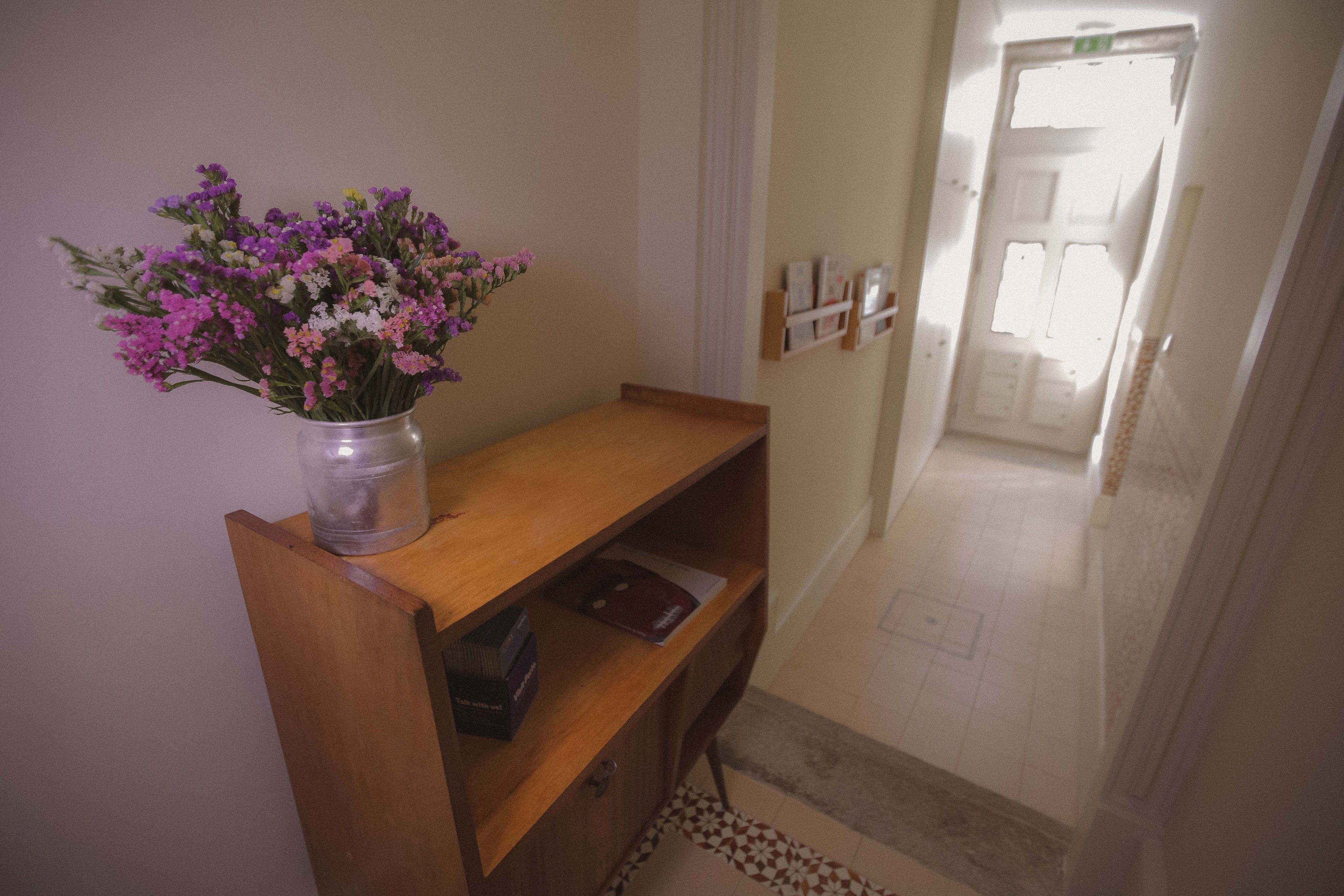 A hallway with a wooden bench, a vase of flowers, and a door at the end.
