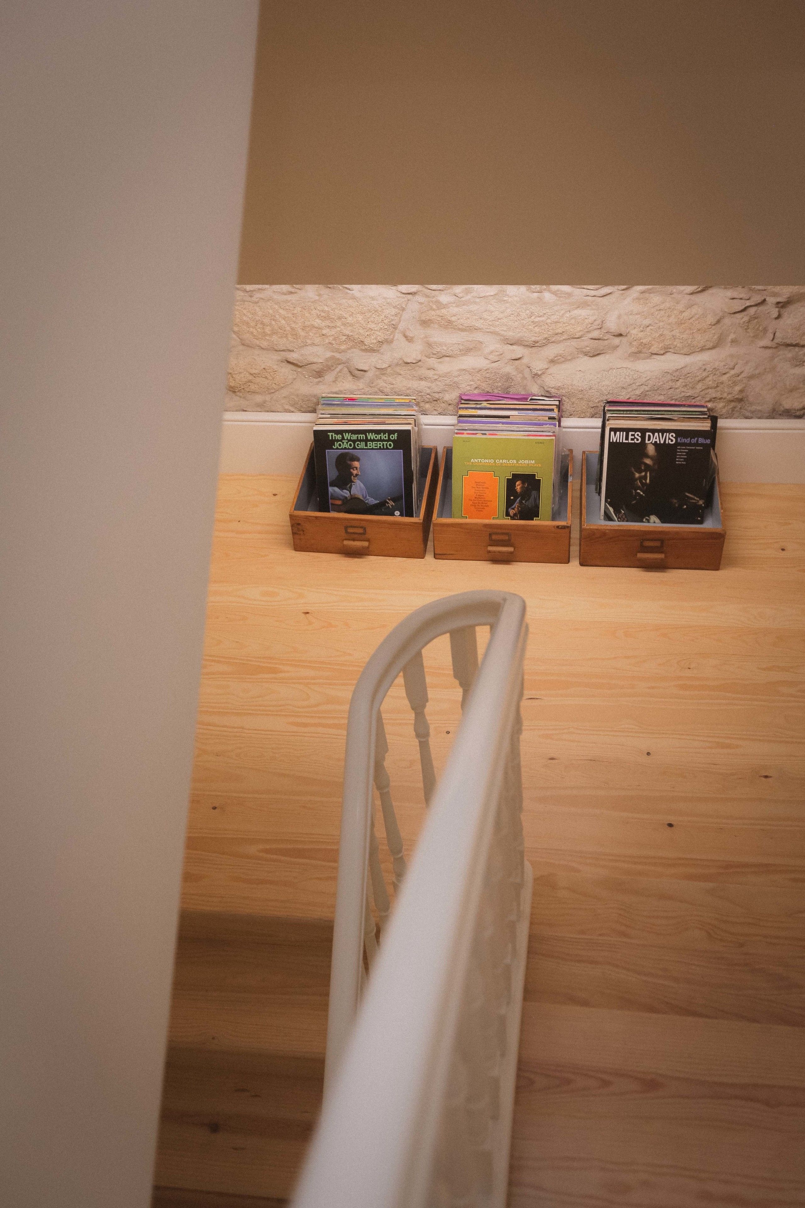 A staircase with a white railing leading to a room. There are three wooden storage boxes on the floor, each containing books.