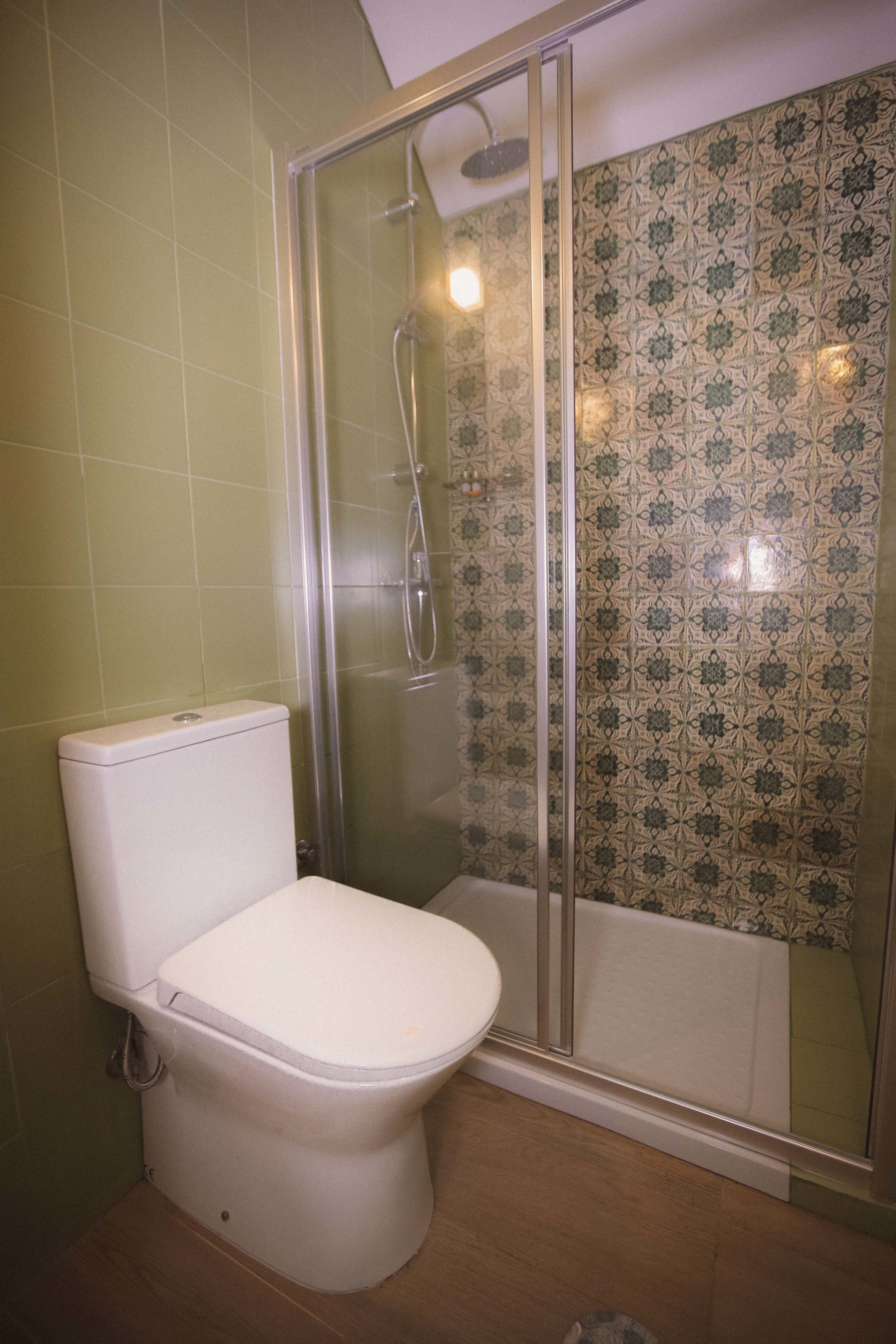 Casa de banho com sanita, cabine de duche e azulejos estampados.