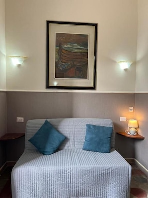Una habitación con una cama, dos almohadas, una obra de arte enmarcada en la pared y dos lámparas de pared.