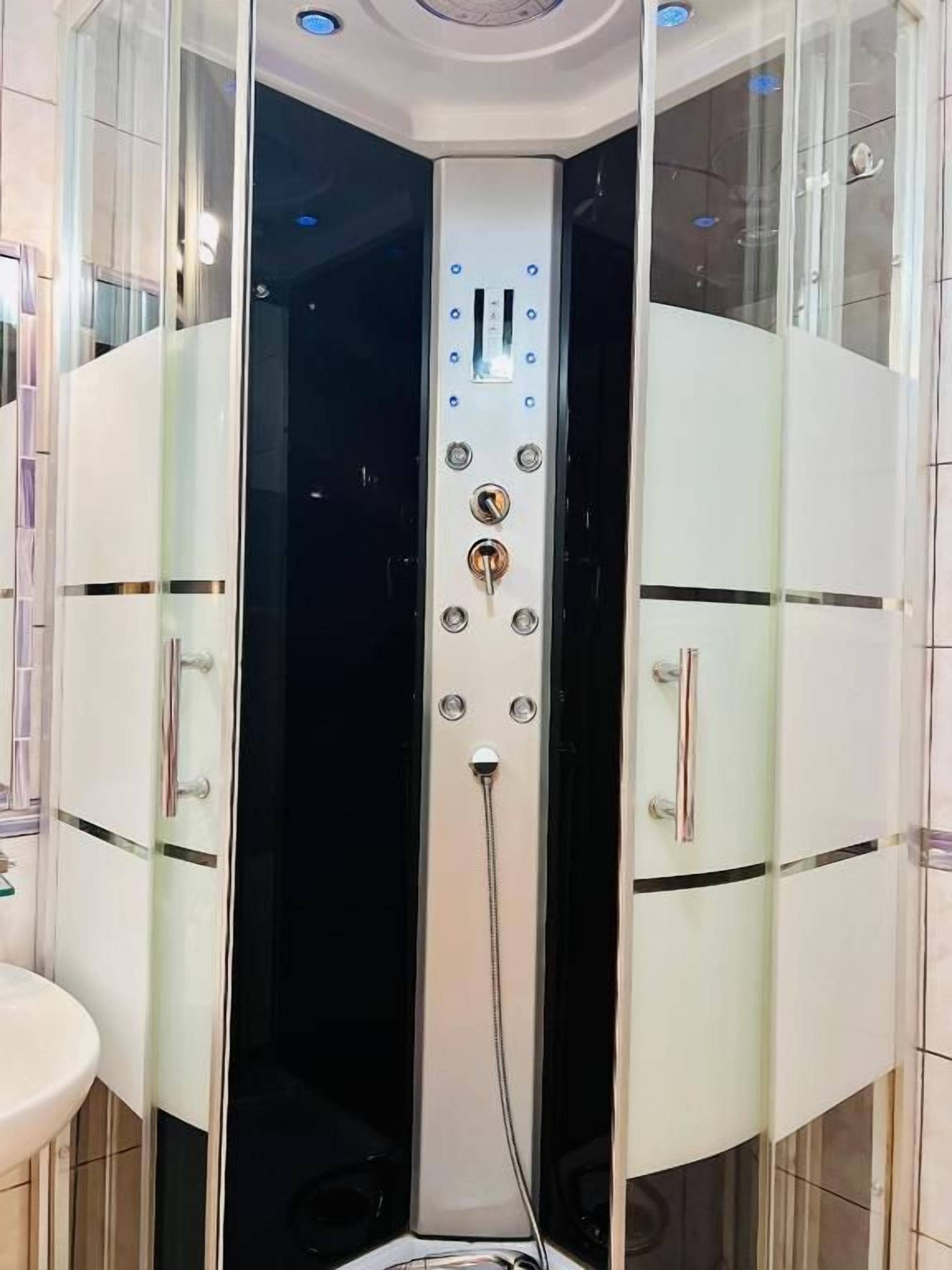 A corner shower enclosure with a control panel, a sink, and a glass door.