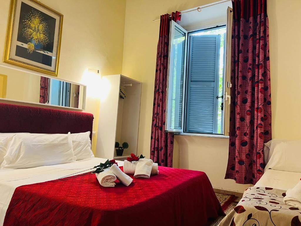 A hotel room with a bed, a window with curtains, a wall-mounted picture, and a bedside table with a lamp.