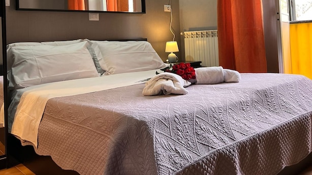 Una cama bien hecha con cubrecama acolchado, una lámpara de noche y un ramo de rosas rojas.
