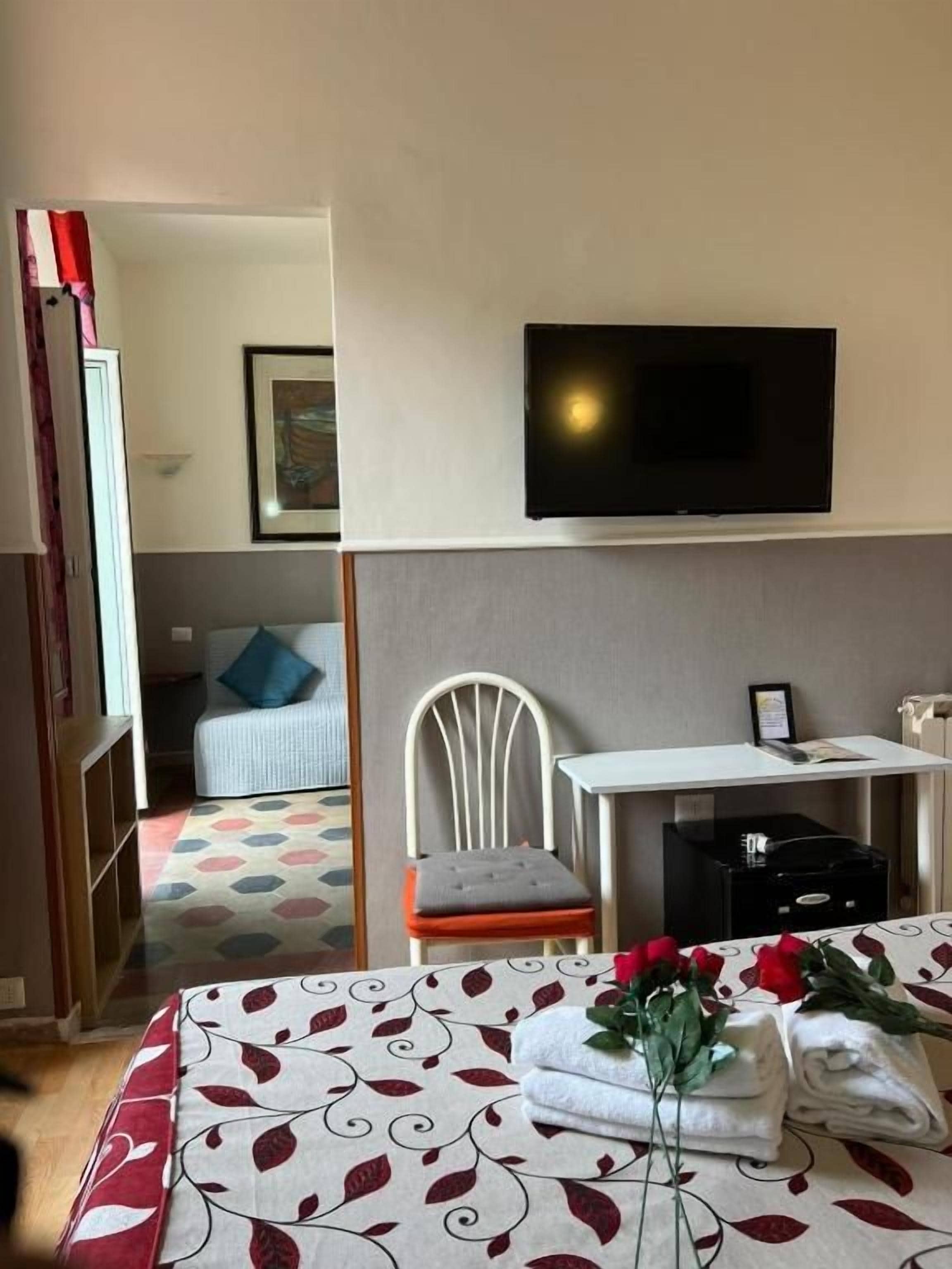 A hotel room with a bed, a flat-screen TV mounted on the wall, a small table, and a chair.