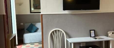A hotel room with a bed, a flat-screen TV mounted on the wall, a small table, and a chair.