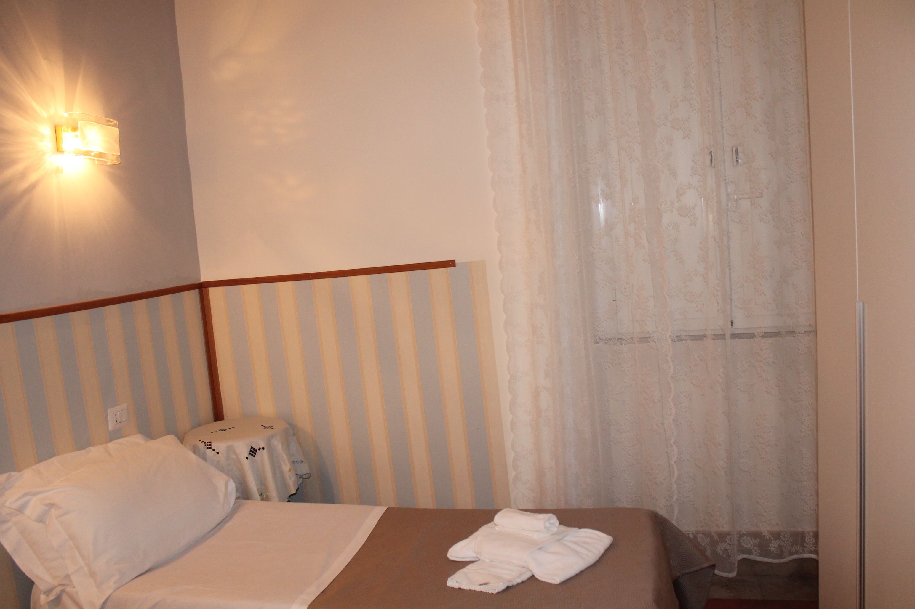 A hotel room with a bed, a bedside table, a lamp, and a window with curtains.