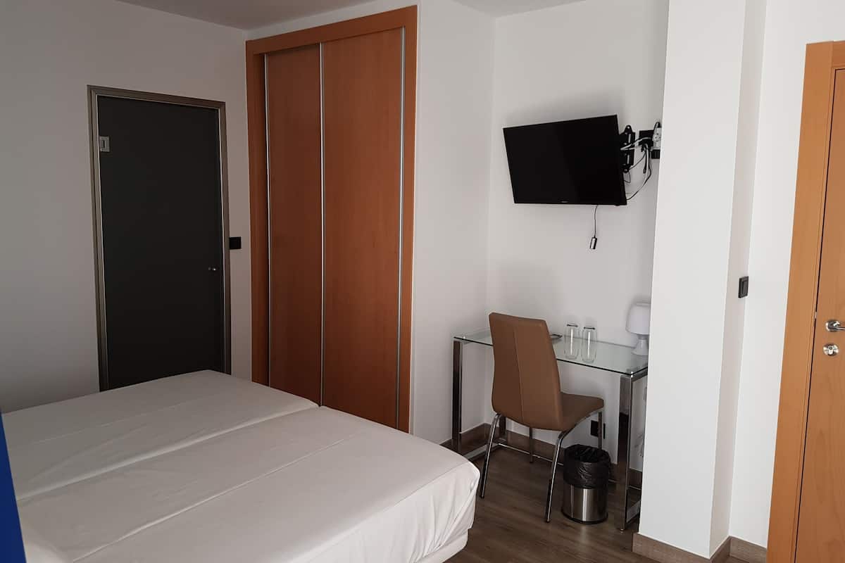 Une chambre d’hôtel comprenant un lit, un bureau avec une chaise, un téléviseur fixé au mur et une armoire.