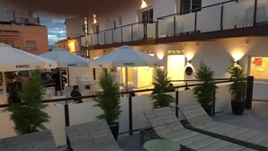 Eine Dachterrasse mit Holzliegen und Tischen, umgeben von Topfpflanzen.