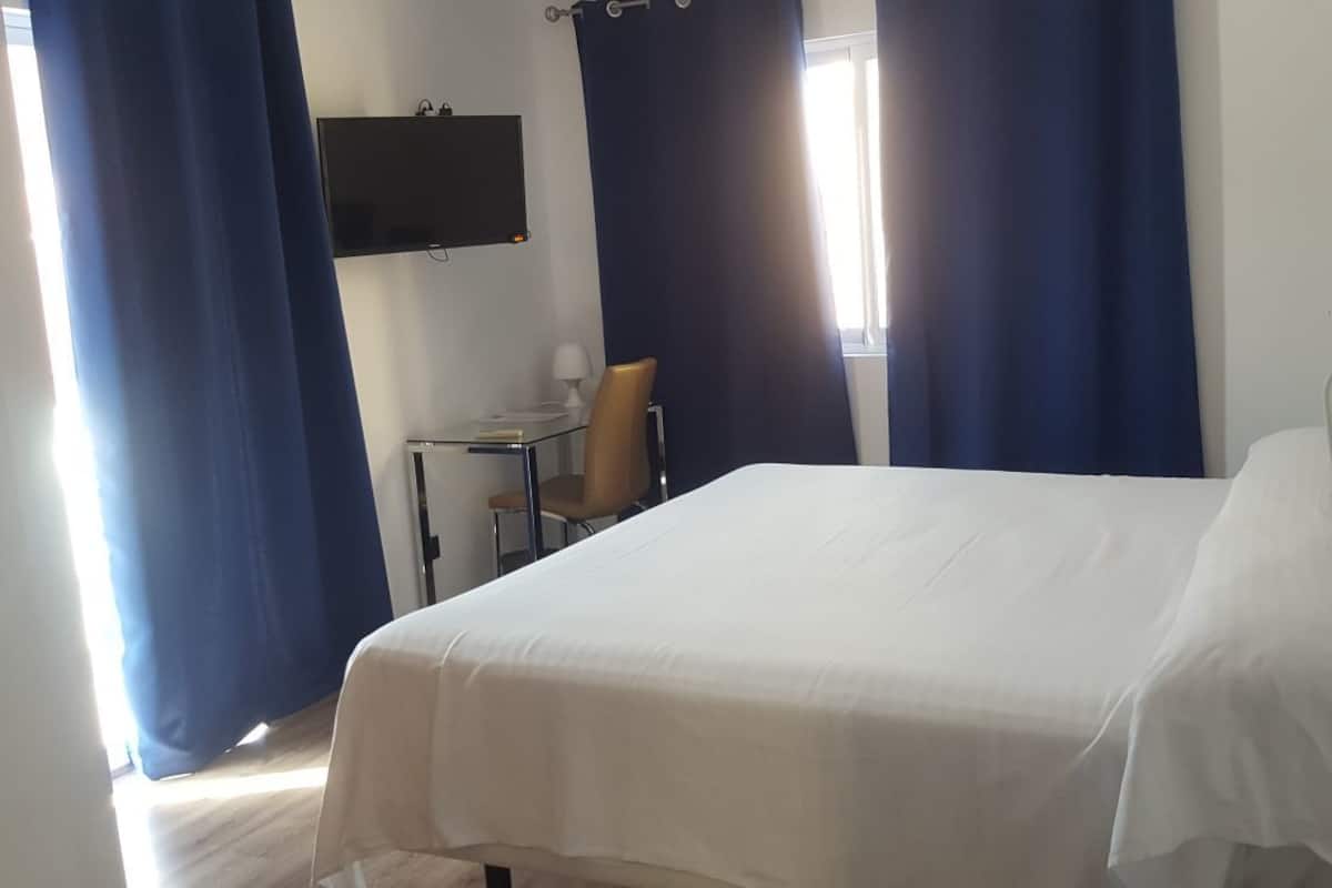Une chambre d’hôtel avec un lit, un bureau, une chaise, une télévision et des rideaux.