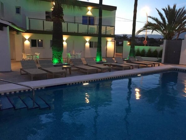 A swimming pool with lounge chairs and a building with illuminated pillars. - Hotel Moli Boutique (L'Alfas del Pi)