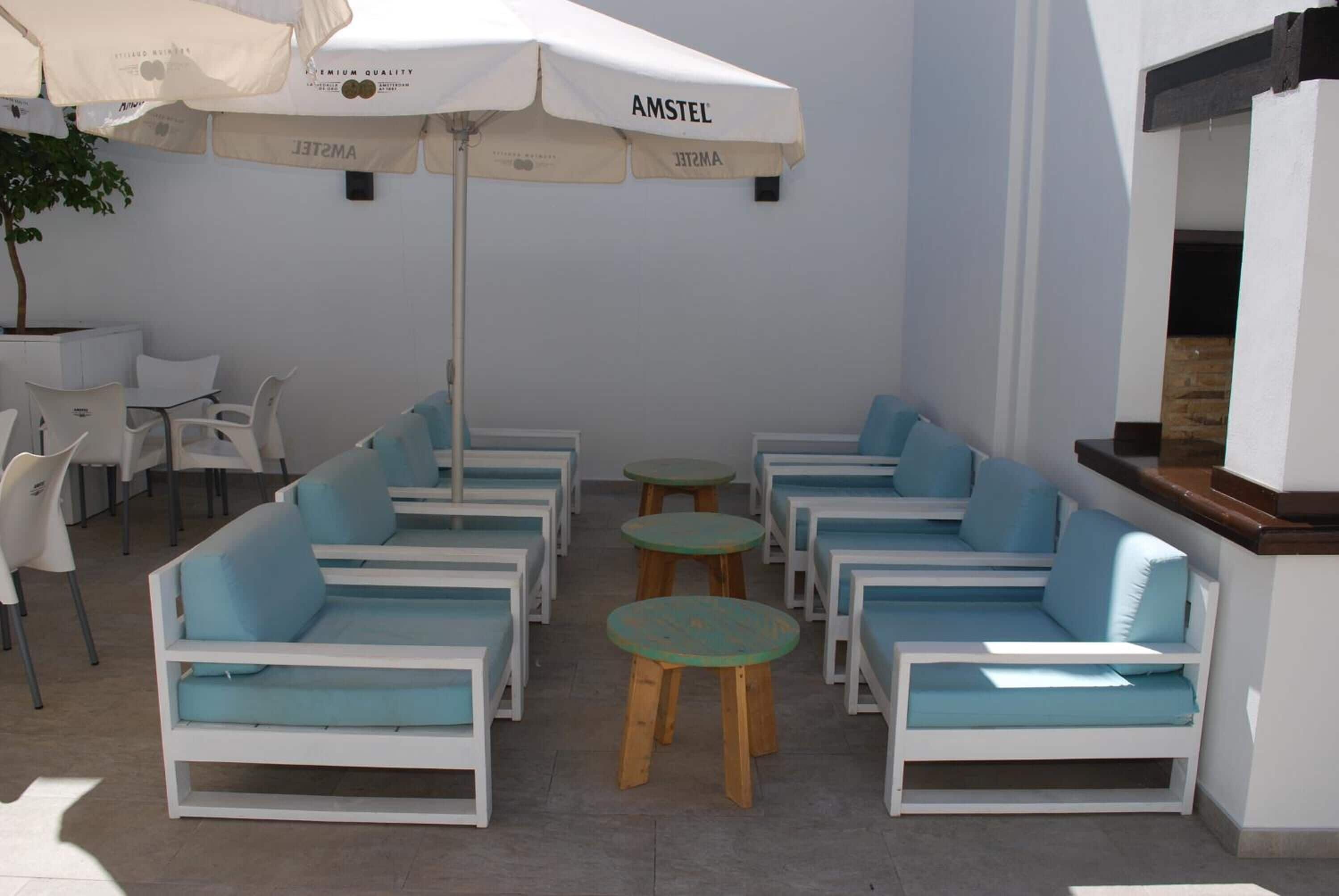 A seating area with white sofas and blue cushions, arranged around small round tables, under a large umbrella labeled "AMSTEL".