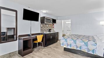 A modern hotel room with a bed, a desk with a chair, a flat-screen TV, a microwave, and a tiled backsplash.