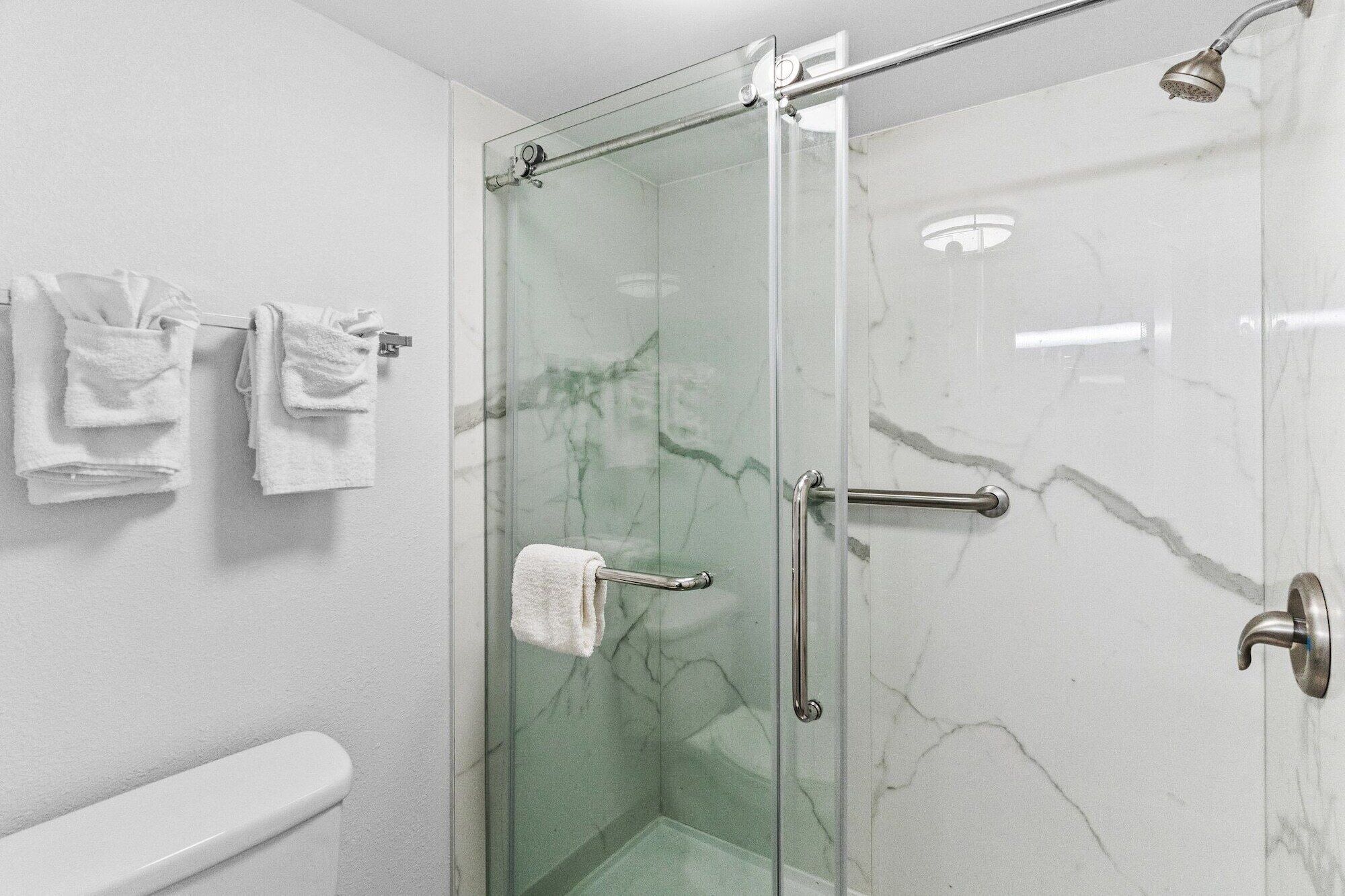A glass-enclosed shower with a handheld showerhead, a glass door, and a towel rack with folded towels.