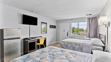 Habitación de hotel con dos camas, un escritorio, una silla, un televisor y una ventana con vistas.