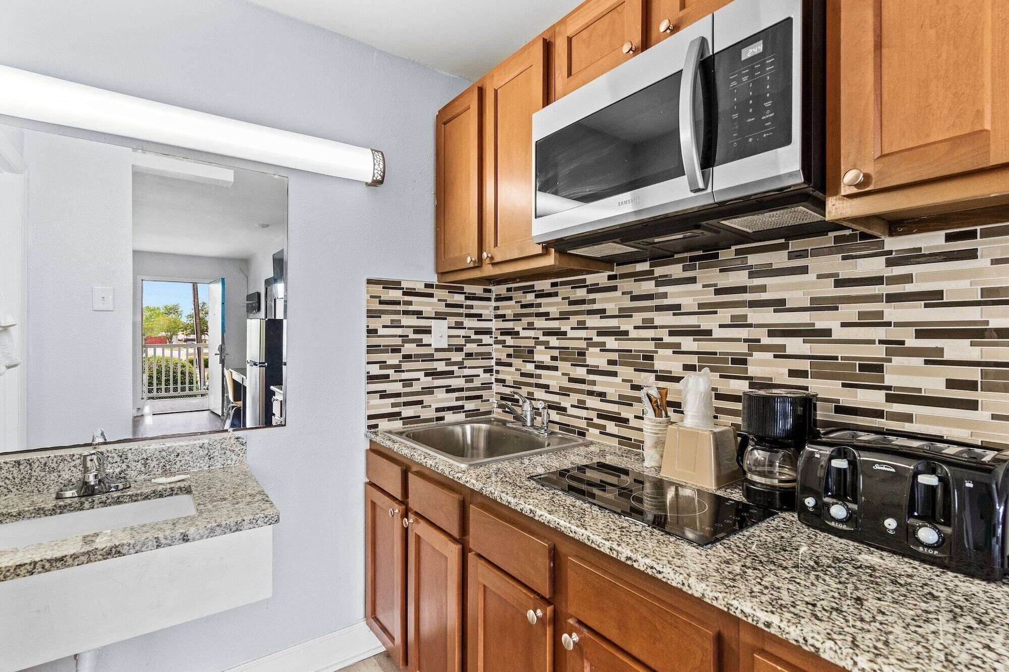 A modern kitchen with wooden cabinets, a stainless steel microwave, a granite countertop, and a tiled backsplash.
