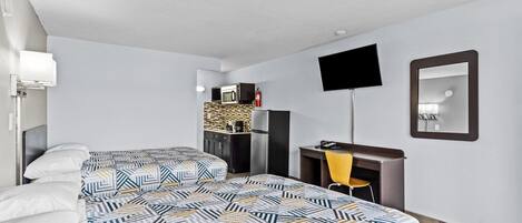 A hotel room with two beds, a desk, a chair, a TV, and a kitchenette.