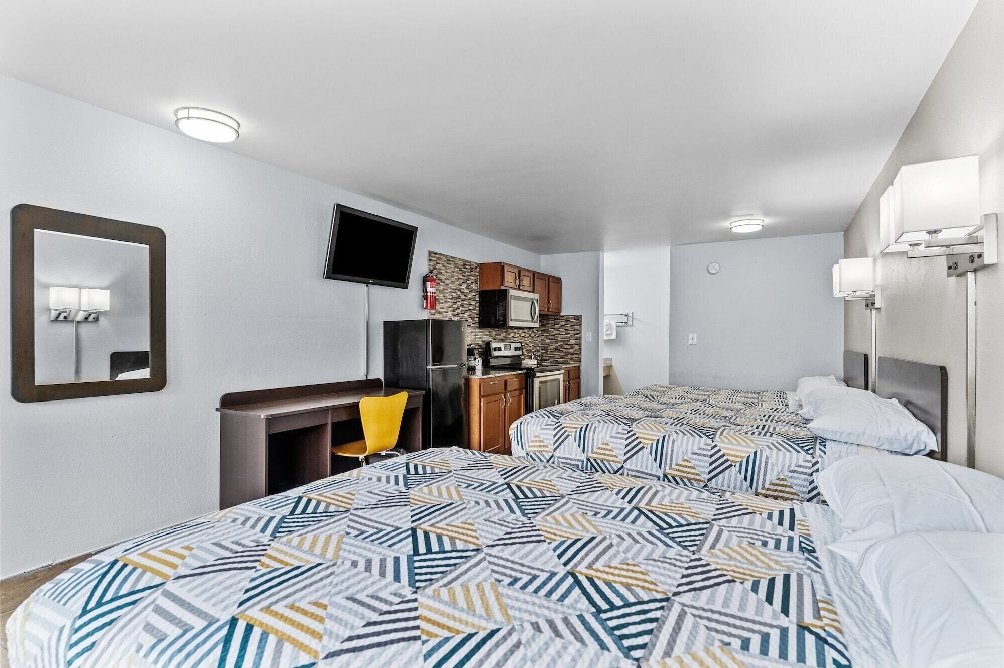 A hotel room with two beds, a desk, a TV, a microwave, and a small kitchenette.