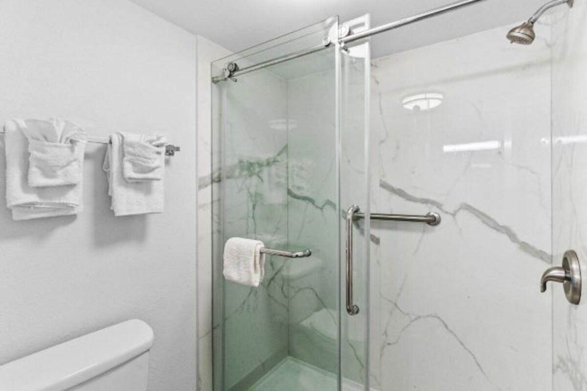 A glass-enclosed shower with a glass door, a white toilet, and a towel rack with folded towels.