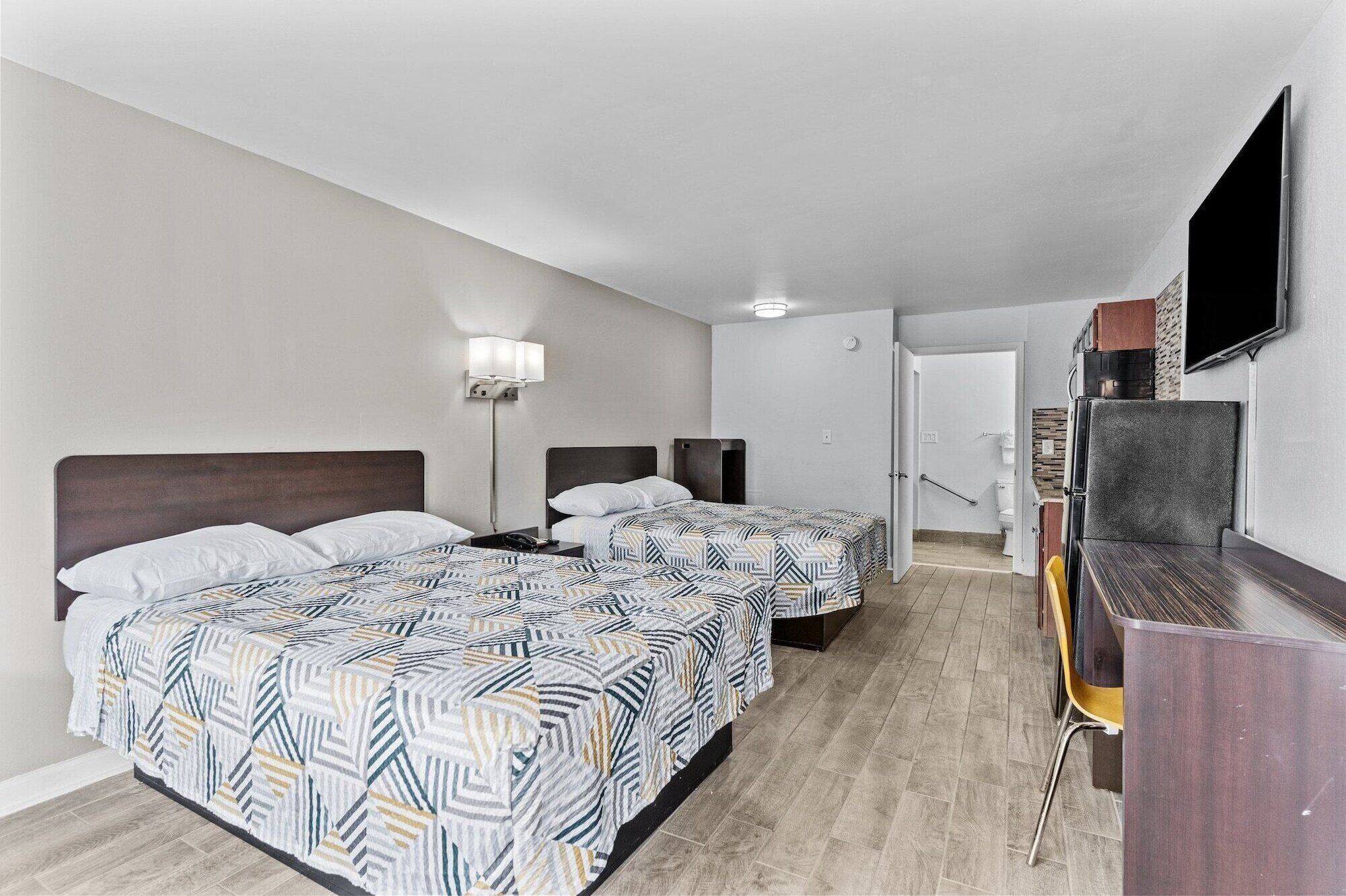 A hotel room with two beds, a desk, a TV, and a bathroom visible through an open door.