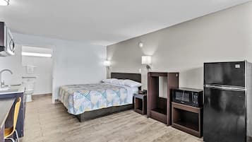 A compact hotel room with a bed, a small desk with a chair, a microwave, and a refrigerator.