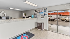 A reception area with a counter, a trash bin, and a glass door leading outside. - Studio 6 Wilmington, NC (Wilmington)