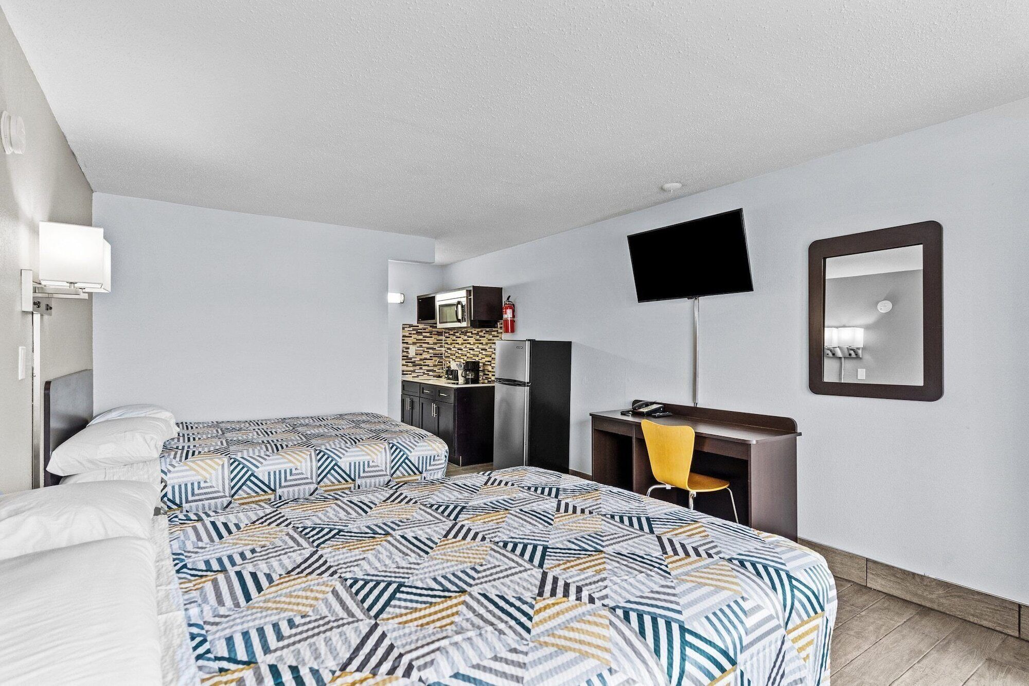 Une chambre d’hôtel avec deux lits, une kitchenette, un bureau avec une chaise, un téléviseur à écran plat et un miroir.