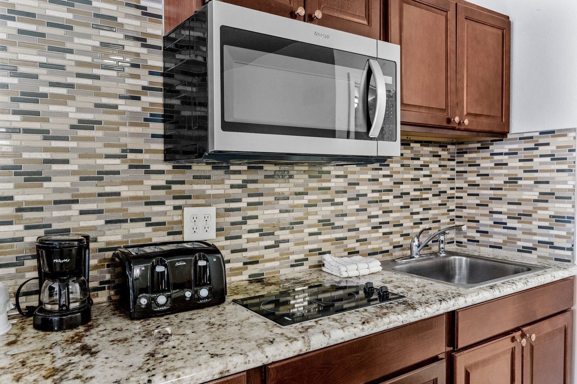 A kitchen with a microwave, coffee maker, toaster, sink, and granite countertop.