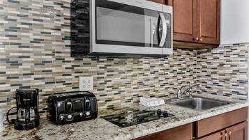 A kitchen with a microwave, coffee maker, toaster, sink, and granite countertop.