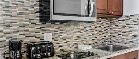 A kitchen with a microwave, coffee maker, toaster, sink, and granite countertop.