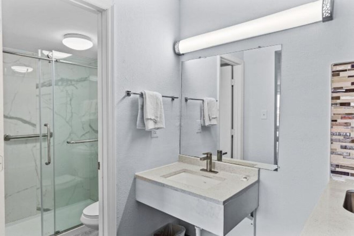 A modern bathroom with a glass shower enclosure, a white sink with a mirror above it, and a tiled backsplash.